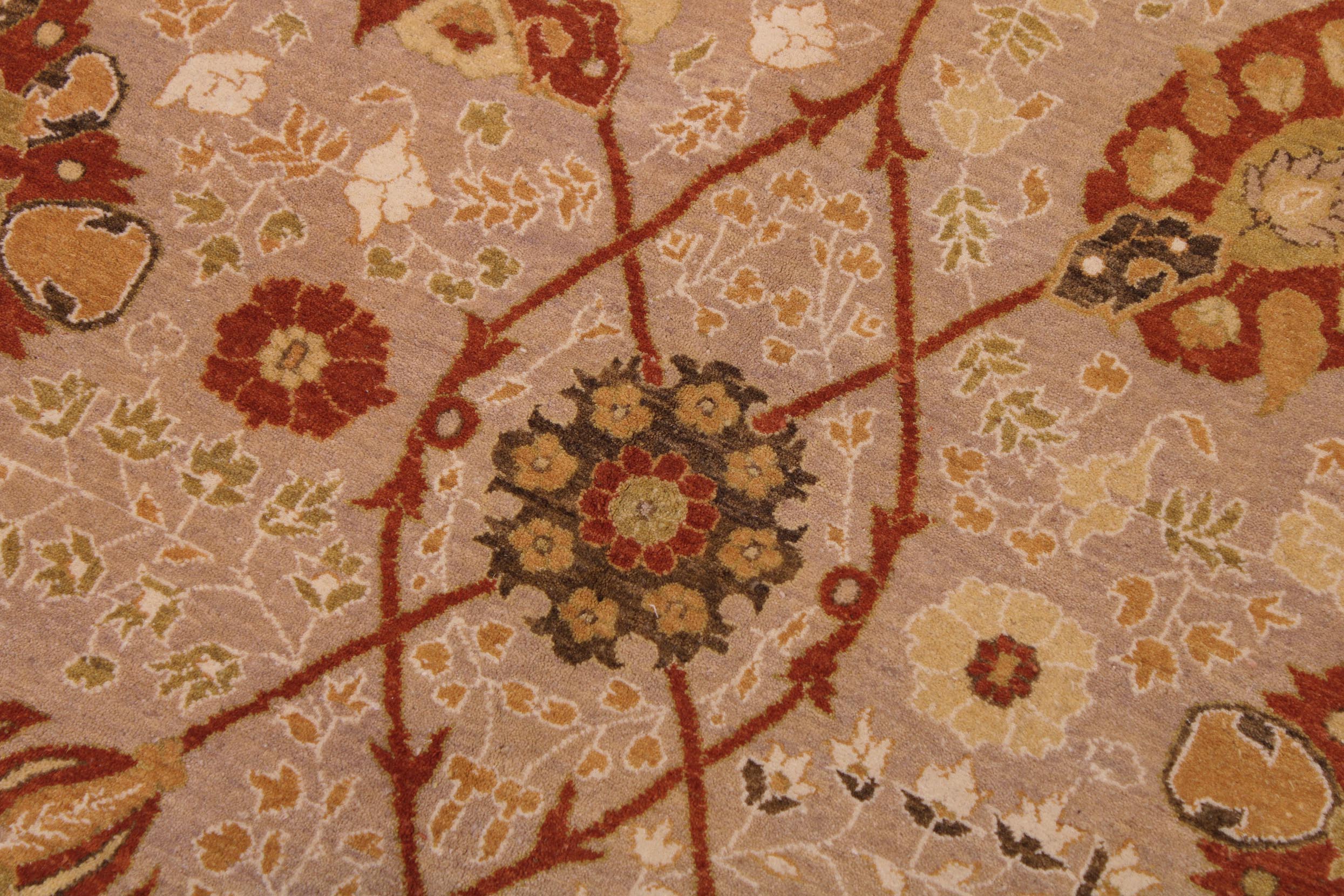 A close-up of a patterned textile or rug showing a beige background with red, rust, olive green, and cream floral and geometric motifs.